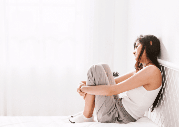 woman sitting on bed knees pulled in sad