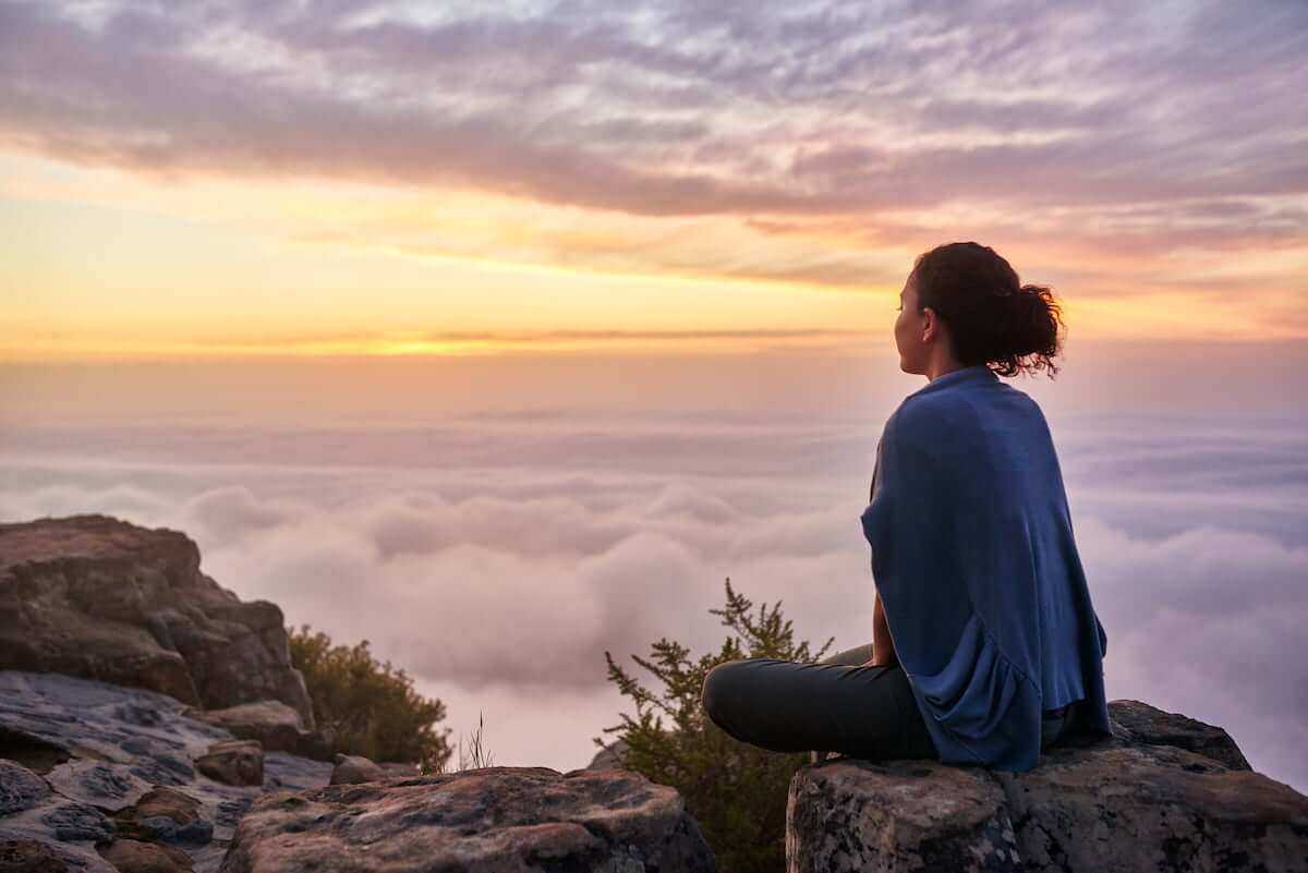 Woman sitting on a rock, a sunset and clouds in the background